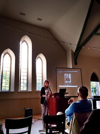Lori Oschefski at lecturn delivering a talk, with presentation projected on screen behind her